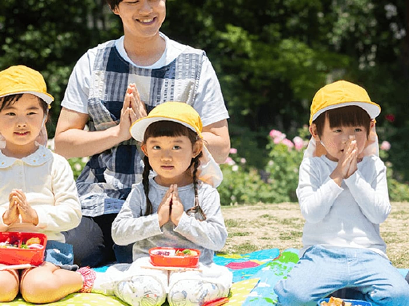 園庭でお弁当を食べる子どもたちと保育士
